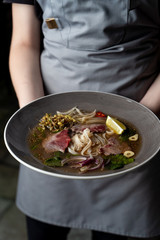 Holding a bowl with raw beef tenderloin soup with rice noodles, onion, garlic, chilli pepper, seedlings and mint