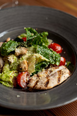 Close up of classic caesar salad with grilled chicken fillet, greens and cherry tomatoes in daylight