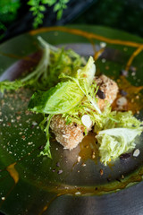 Close up of deep fried Camembert with waffle crumbs, sweet sauce, grated nuts and greens