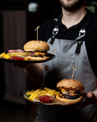 Waiter is holding trays with marble beef burger with cheese sauce and hot french fries