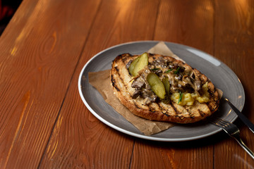 Ciabatta toast with fried button mushrooms, pork and pickled cucumbers on rustic wooden background