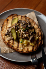 Ciabatta toast with fried button mushrooms, pork and pickled cucumbers on rustic wooden background