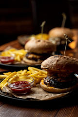 Close up side view of marble beef burgers with cheese sauce and hot french fries on wooden table