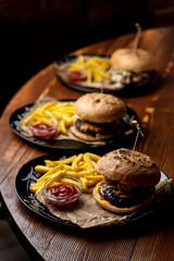 Close up side view of marble beef burgers with cheese sauce and hot french fries on wooden table