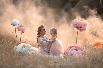 Mom and daughter in pink fairy-tale dresses play in a field surrounded by Big pink decorative...