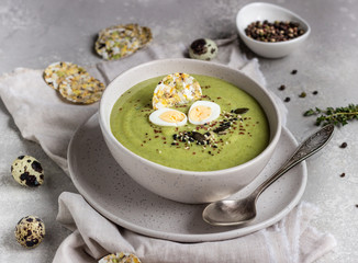 Detox broccoli green cream soup with seed mix, quail egg and crackers in bowl on light grey stone background. Healthy food concept.