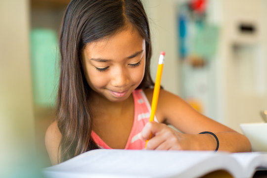 Young Girl Sitting At A Desk And Working On Her Homework
