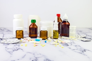 Many different vials and jars with pills and drugs of different colors and sizes on a white marble background. Medical background