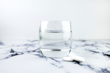Effervescent tablets and glass with water. Fast dissolving medicine on white marble background