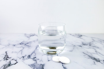 Effervescent tablets and glass with water. Fast dissolving medicine on white marble background