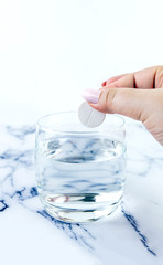 A hand throwing a medicine into a glass quickly dissolves. The effervescent tablets and glass with water