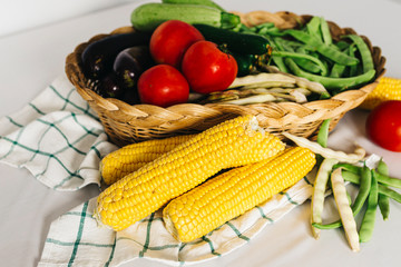 a group of fresh vegetables in a basket, there are tomatoes, zucchini, eggplant, yellow and red bean, cucumber and corn