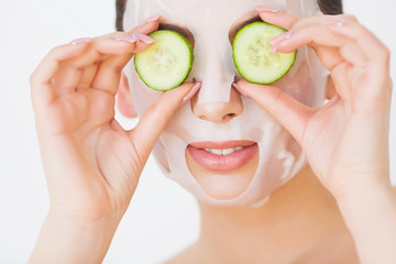 Beautiful young Woman in clay mud mask on face covering eyes with slices cucumber.