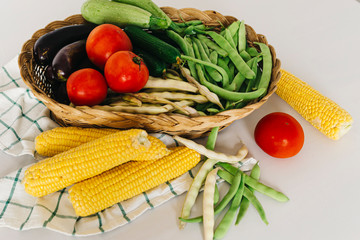 a group of fresh vegetables in a basket, there are tomatoes, zucchini, eggplant, yellow and red bean, cucumber and corn