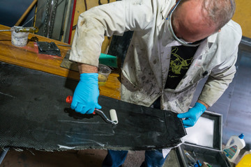 Man with protections on hands, eyes and mask, repairing a piece of carbon and epoxy resin.