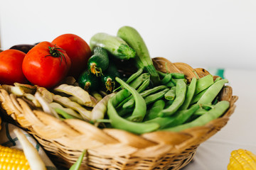 a group of fresh vegetables in a basket, there are tomatoes, zucchini, eggplant, yellow and red bean, cucumber and corn