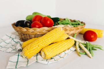 a group of fresh vegetables in a basket, there are tomatoes, zucchini, eggplant, yellow and red bean, cucumber and corn