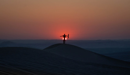 A man whit a skateboard in her hand, the desert with a beautiful sunset