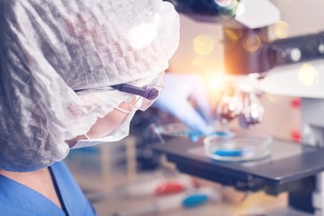 Female scientist in mask and glasses working with microscope