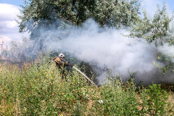 Fototapeta premium fireman in a protective suit in a cloud of smoke under burning pressure burning garbage in a natural landfill environment.