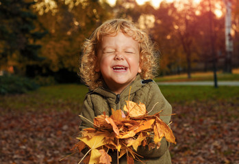 Cute little child smiling and holding orange foliage in the park 