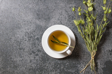 White cup of herbal sage tea with dried sage leaves on grey rustic background. Herbal tea hot drink concept,  Salvia officinalis