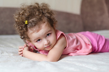 Fototapeta premium portrait of a little adorable cute girl with curly hair on a pink and grey background. happy childhood. beautiful baby posing and look at the camera.