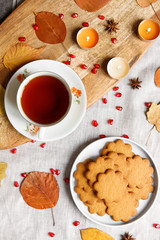 Top view of a cozy homemade tea party.  Autumn composition. Cup of hot tea, Gingerbread cookie, burning candles, yellow fallen leaves, seeds pomegranate, anise on a linen tablecloth. Flat lay