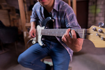 Obraz premium young man playing guitar in a garage making the major sun chord