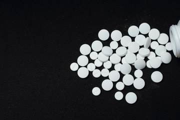 A large number of white tablets scattered from the container on a black background. concept of illness, depression, suicide. pharmaceutical pills for illness and pain. top view