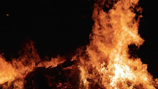 A large crowd of people celebrate an ethnic holiday by a giant bonfire. Burning red hot sparks rise from large fire in the night sky. Belarusian Kupalle. Russian ethnic holiday Ivan Kupala in village.