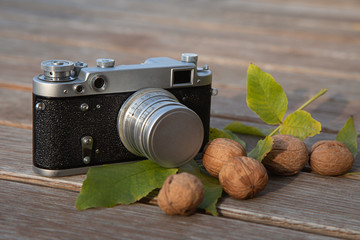 Still life autumn mood picture with vintage rangefinder camera, leaves and nuts on wooden background
