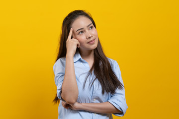 Cute asian woman in casual dress thinking and imagination isolated on yellow background