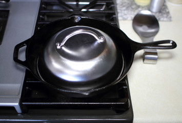 Stainless steel melting dome in a cast iron skillet on the stove in a home kitchen.