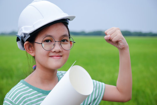 A young Asian girl engineer wearing a white safety hat holding a paper roll.