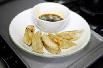 Pan fried dumplings with soy dipping sauce on a plate, resting on the stove top in a home kitchen.