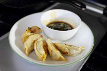 Pan fried dumplings with soy dipping sauce on a plate, resting on the stove top in a home kitchen.