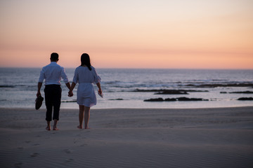 Fototapeta na wymiar Couple holding hands and walking on beach during sunset