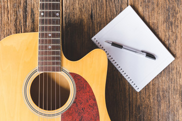 Fototapeta premium Top view of Acoustic guitar , Notebook paper and pen on wood background and copy space