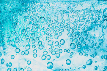 transparent background of soda water and ice with bright blue bubbles within the glass is abstract.