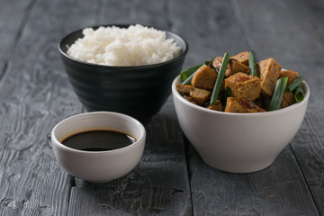 A bowl of rice and a bowl of tofu cheese on a wooden table.