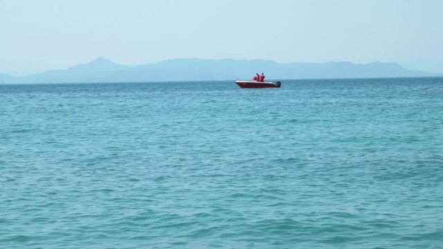 Small Motor Boat on light blue sea with mountains in the background