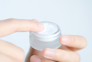 Hand of woman holding moisturizer cream and serum. She applying a facial cream , essential , oil , lotion and body cream for skin care, close up view and blur background. Beauty and Healthy Concept.