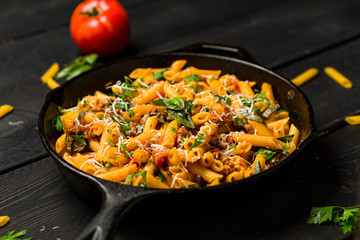 Pasta on dark background. This quick & delicious pasta meal is made with penne pasta, fresh tomato sauce and sausage. This italian inspired comfort food is cooked and served in a cast iron skillet.