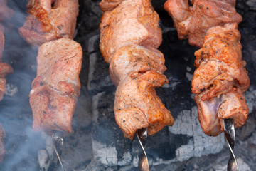 skewers of meat with smoke is cooking on the coals