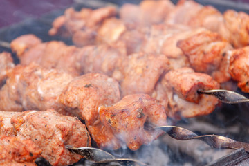 skewers of meat with smoke is cooking on the coals