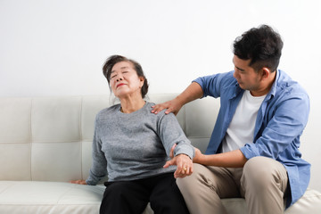 Asian senior woman mother and young man son in blue shirt massage his mother in living room