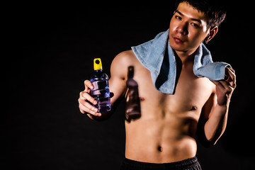 Fototapeta premium sport man standing holding a towel and bottled water on black backgrounds, fitness concept, sport concept