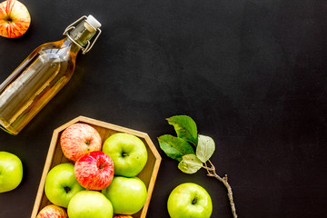 Apple cider in bottle near tray with fruits on black background top view copy space