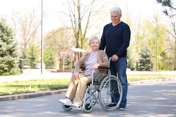 Senior woman in wheelchair and mature man at park on sunny day
